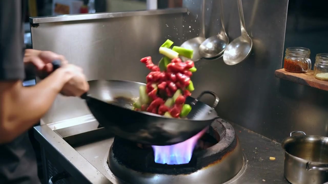 Tossing black-shirt cook flipping meat, veg at kitchen wok, to sear and mix, salt visible