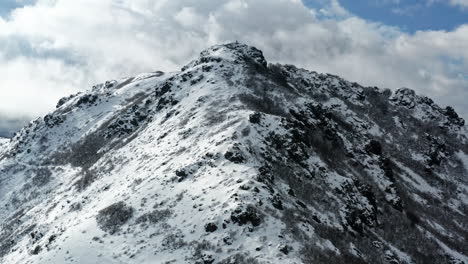 Snow-covered-mountain-peak-under-a-cloudy-sky,-showcasing-rugged-terrain-and-natural-beauty,-aerial-view