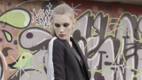 stylish woman in a black blazer with white fringe, posed against a graffiti wall