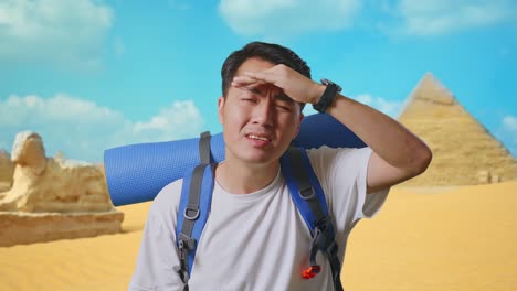 close up of asian male hiker with mountaineering backpack hand forehead smiling and looking distance while traveling in pyramid of giza