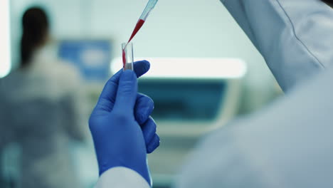 Close-Up-Of-The-Glass-Test-Tube-With-A-Blood-In-It-In-Hands-In-Medical-Gloves-Of-The-Man-Or-Woman-While-They-Doing-Analysis-In-The-Laboratory