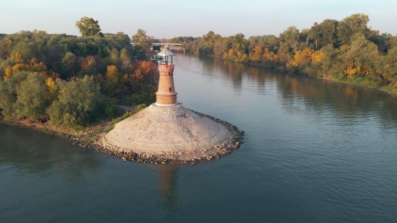 drone aéreo orbitando alrededor del antiguo faro de piedra en el río danubio en un soleado día de puesta de sol de otoño