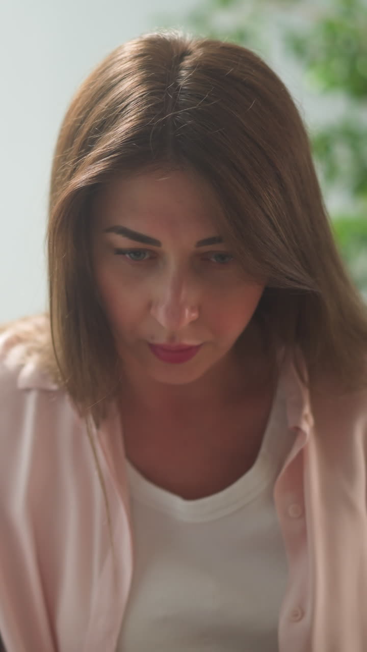 Concentrated brown-haired woman in casual clothes looks downward sitting with kid on sofa closeup slow motion. Lady plays board game by floor lamp. Domestic lifestyle