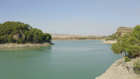 rocky shores of lake caminito del rey with pine trees,wind farm beyond