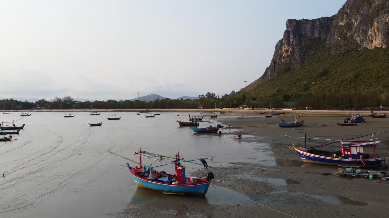 antena: barcos de pesca asiáticos varados en la marea baja en la costa con montañas rocosas en el fondo en tailandia