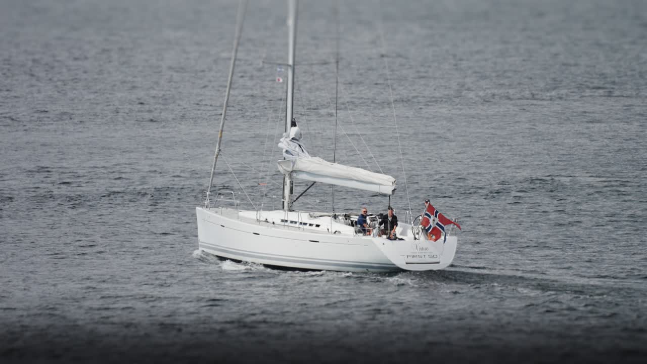 A sailboat with a folded sail and a Norwegian flag goes under the motor