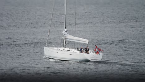 a sailboat with a folded sail and a norwegian flag goes under the motor