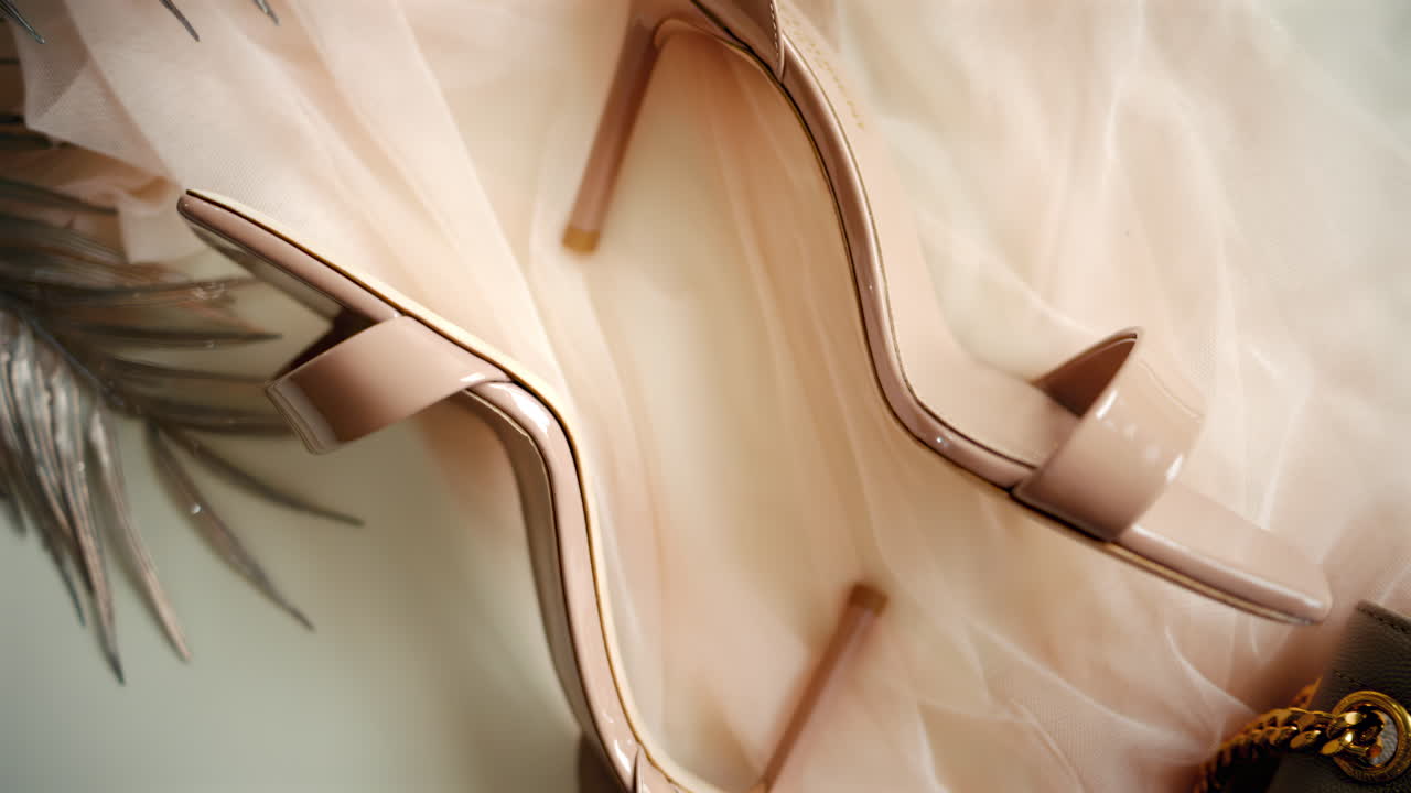 A beige pair of strappy heels near a bag on a piece of tulle