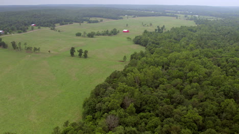 aerial of farmland and trees in southern missouri with a red barn trucking right