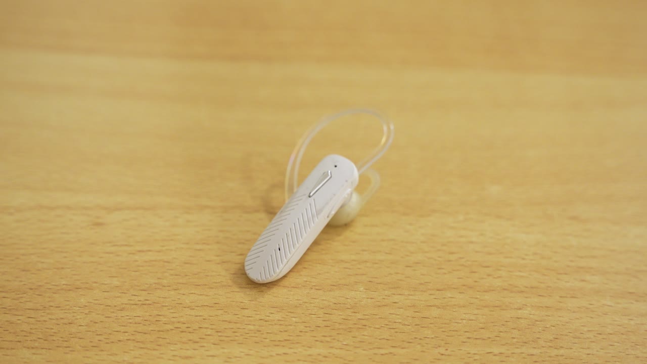 Classic white bluetooth earpiece resting on wooden table - retro wireless tech for calls, mobile and songs.