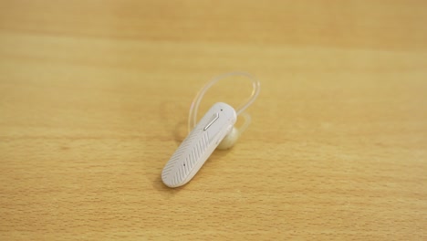 classic white bluetooth earpiece resting on wooden table - retro wireless tech for calls, mobile and songs.