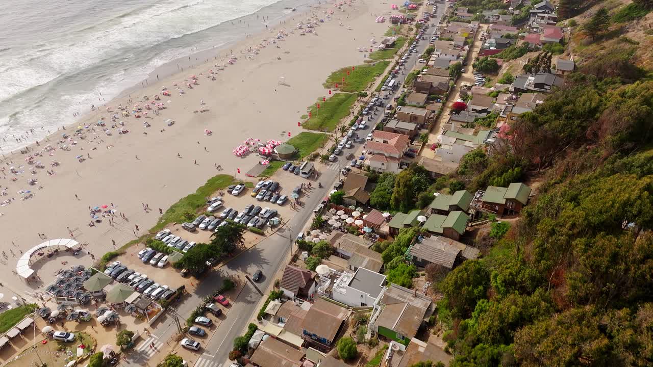 vuelo aéreo sobre casas cerca de la playa de maitencillo con bañistas y sombrillas coloridas