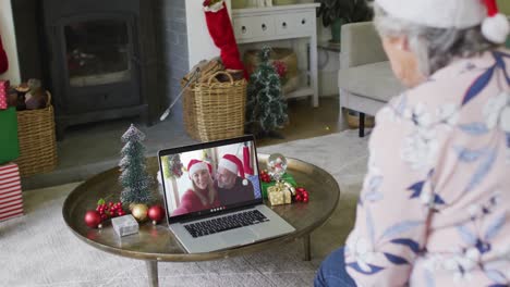 Caucasian-senior-woman-using-laptop-for-christmas-video-call-with-smiling-couple-on-screen