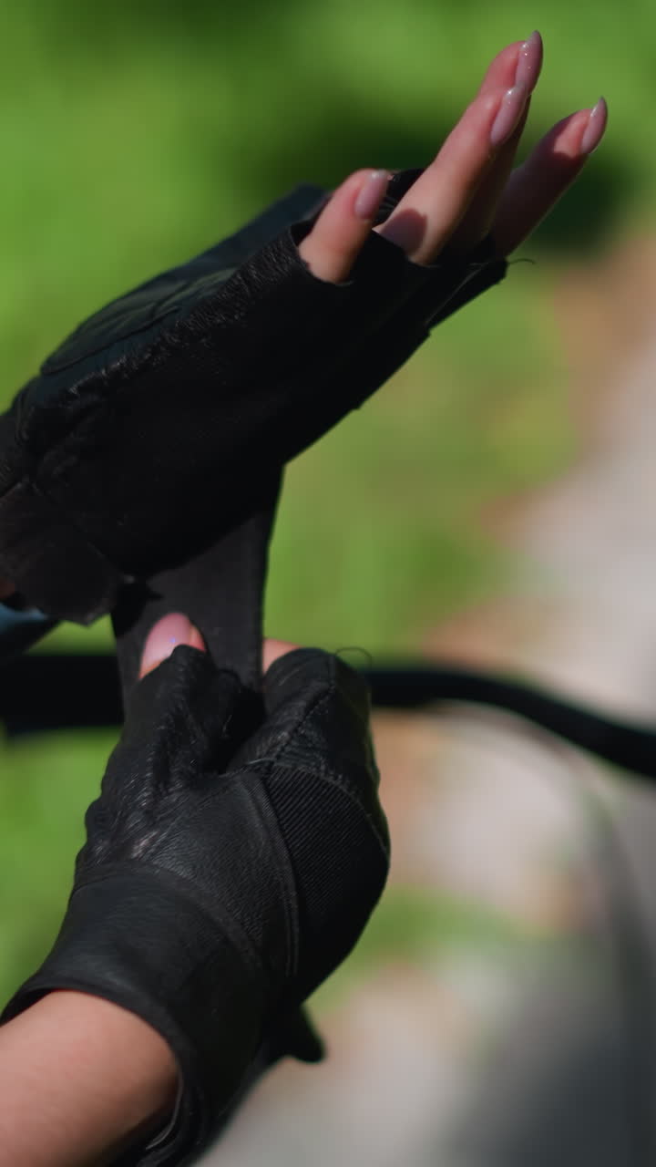 자전거 근처의 왼쪽 손에 개인을 확보하는 바이커 장갑의 근접 후면 뷰, 손가락에 초점을 맞추고 흐릿한 배경으로 울창한 초록색과 포장 된 경로를 특징으로하는 스트을 조정합니다.