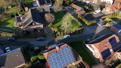 modern single family houses with solar panels on roof at sunny day. winter scene with grass in garden. aerial top down flyover shot. parking cars on hilly street.