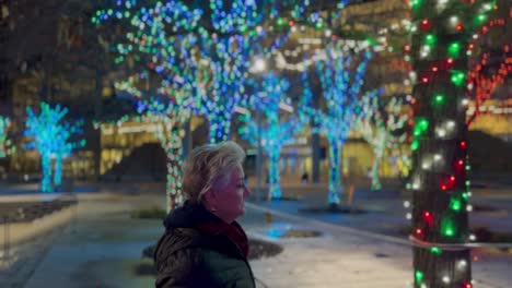 Mujer-Mayor-Caminando-Por-Una-Ciudad-De-Noche-Decorada-Con-Luces-Navideñas