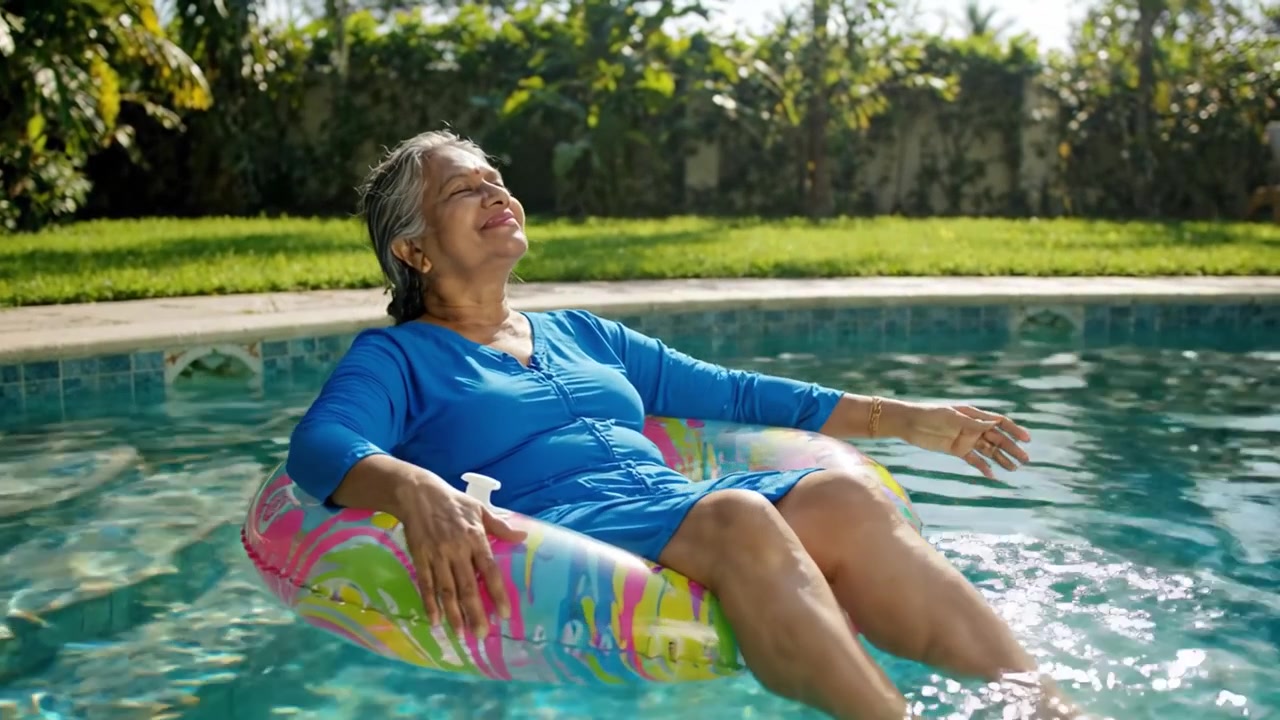Relaxing in the Sun: An Elderly Woman Enjoys a Peaceful Moment Floating in a Colorful Pool Float, Surrounded by Lush Greenery and Tranquil Waters