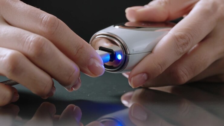 Aligning plug, hands guiding braided cable into silver unit on dark table, charging, blue LED