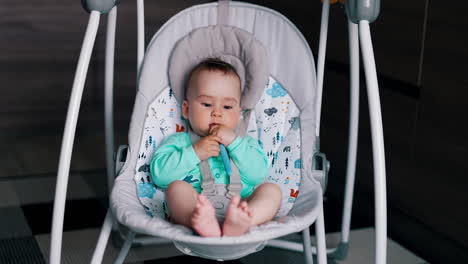 beautiful child sitting in a swaying chair chews the spoon. active healthy baby after feeding.