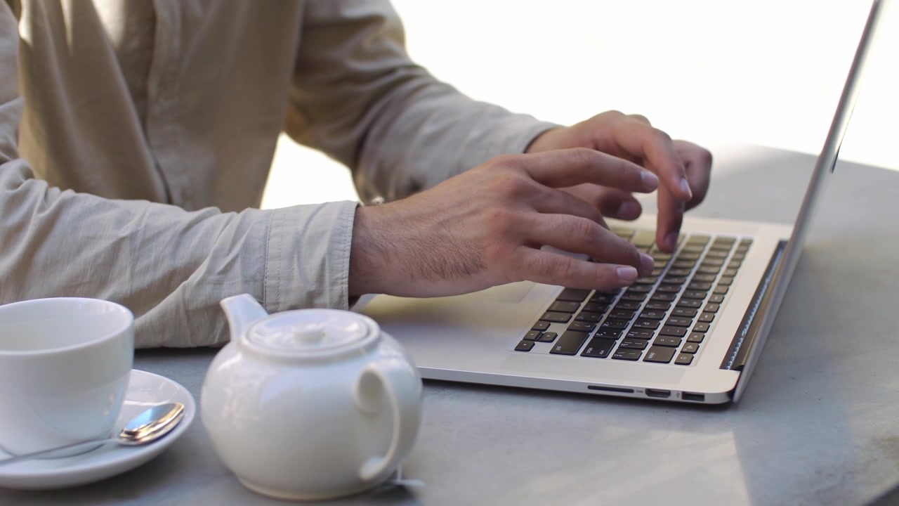 Persona che digita al laptop a un tavolo di un caffè all'aperto