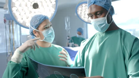 diverse female and male surgeon in masks discussing x ray in theatre, slow motion