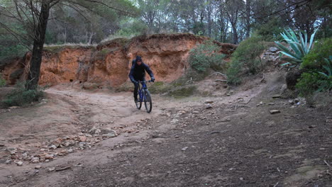 Mountainbiker-Fährt-Eine-Scharfe-Kurve-Auf-Einem-Schroffen-Feldweg,-Der-Sich-Durch-Einen-Dichten-Wald-Schlängelt