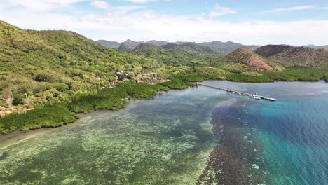 pier on blue coastal waters with lush green hills and forests in busuanga, palawan, philippines, wide aerial shot