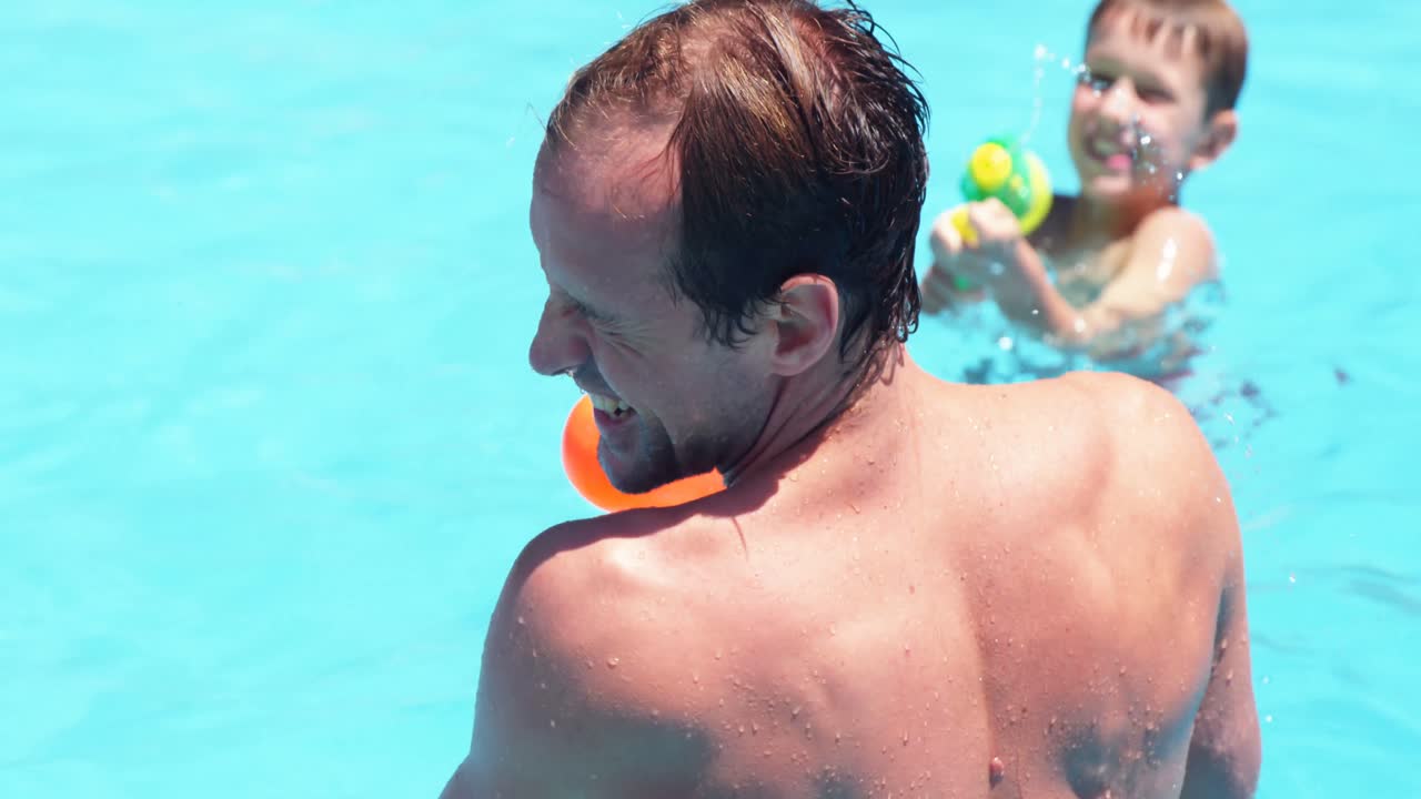 familia feliz haciendo una batalla de pistolas de agua en la piscina