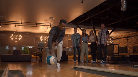 Multi-ethnic-Group-of-friends-in-a-bowling-club-a-black-man-throws-a-ball-and-knocks-out-a-strike