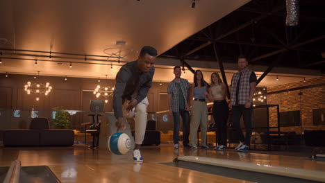 multi ethnic group of friends in a bowling club a black man throws a ball and knocks out a strike