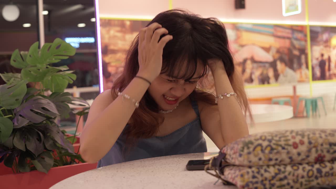 A young woman is sitting indoors, expressing frustration and annoyance in a café