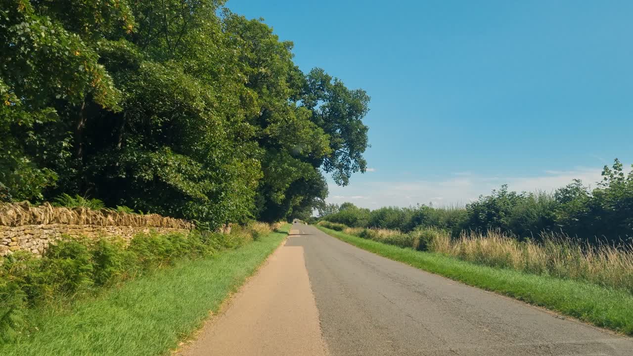 Passenger view from a car driving through the Midlands, UK, showcasing wild and agricultural landscapes under a sunny summer sky
