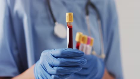 video of biracial female doctor holding test tubes on blue background