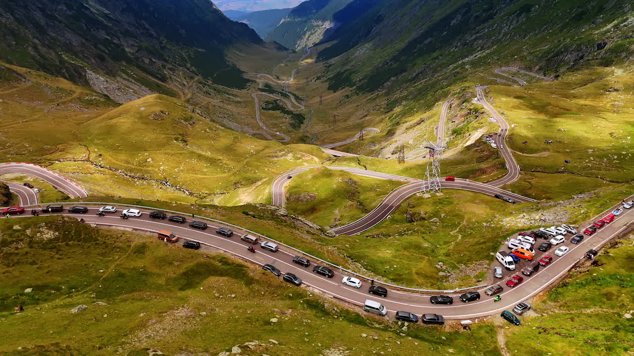 Descending over the part of Transfagarash road with the observation deck on the highway. Multiple cars stand parked to watch the scenery