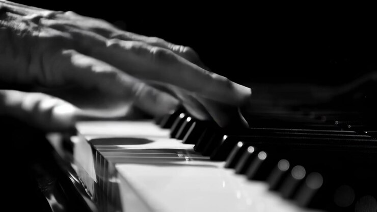 Close-up view shows hands moving over piano keys in rhythmic playing motion, with high contrast black and white lighting, reflective surfaces, and focused composition emphasizing musical expression.
