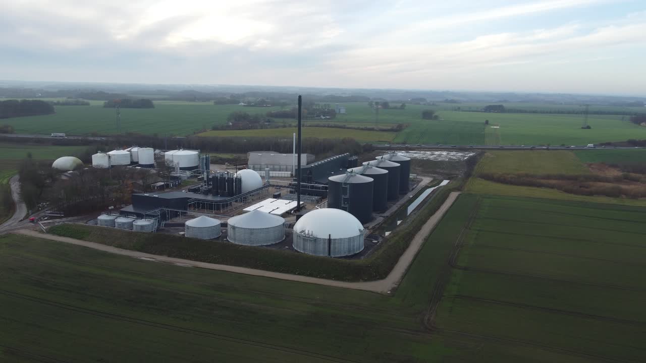 Slow drone push in toward a biogas energy facility in rural Denmark, emphasizing clean energy production and sustainable technology