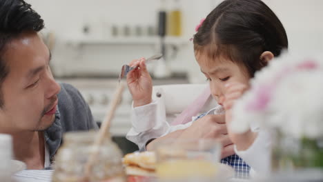 Linda-Niña-Asiática-Desayunando-Padre-Preparando-Gofres-Para-Su-Hija-Disfrutando-De-Una-Deliciosa-Comida-Casera-En-La-Cocina-De-Casa-Preparándose-Para-La-Escuela-4k