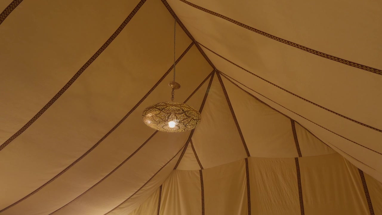 Lampada a sospensione decorativa in ottone filigranato che risplende sotto un caldo soffitto di tenda in tela drappeggiata.