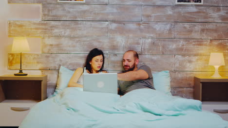 una pareja joven en pijama haciendo compras en una computadora portátil
