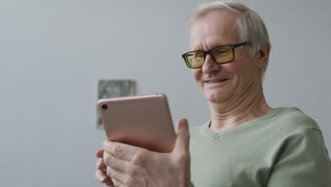 happy senior man using tablet while standing in the living room of a modern apartment