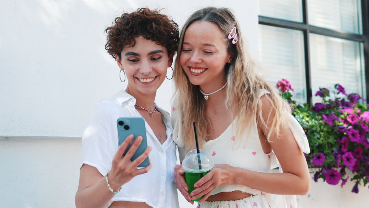 dos mujeres felices usando un teléfono y disfrutando de una bebida