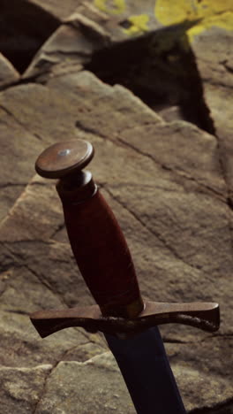 una espada medieval con una empuñadura de cuero marrón, descansando en un entorno rocoso.