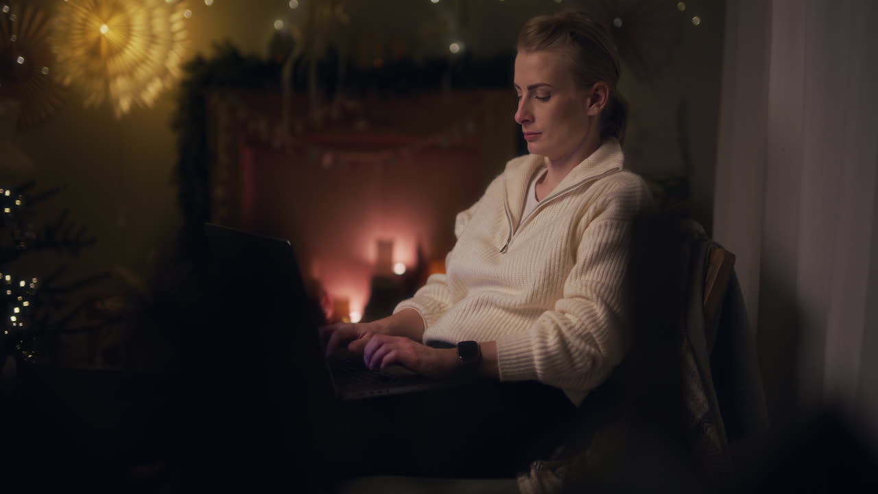 한 여성이 에서 일하며, 벽난로를 배경으로 거실의 의자에 편안하게 앉아 인터넷을 탐색하는 이메일을 쓰고 있습니다.