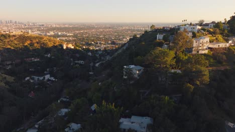 Volando-Sobre-Las-Colinas-De-Hollywood-A-La-Hora-Dorada,-Fincas-De-Lujo-Escondidas-En-Colinas-Boscosas-Con-Una-Puesta-De-Sol-Dorada-En-El-Horizonte