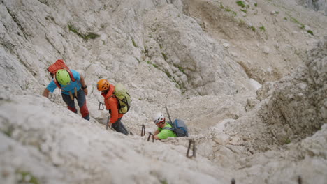 Wanderer-Mit-Helmen-Und-Kleidung-In-Leuchtenden-Farben,-Die-Eine-Felswand-Zum-Gipfel-Des-Berges-Hinaufklettern