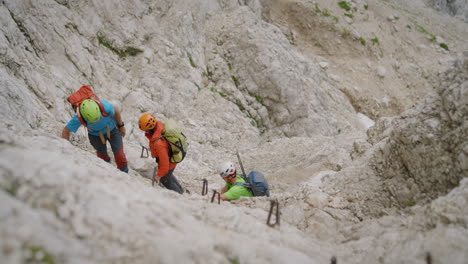 excursionistas con cascos y ropa de colores brillantes trepando por una pared de roca hacia la cima de la montaña