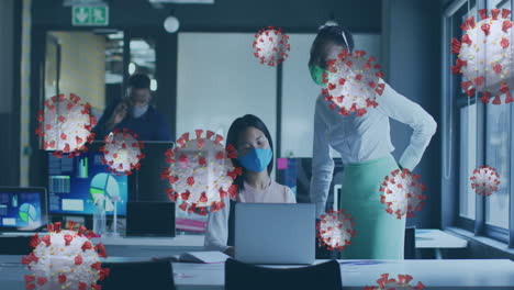 animación de células de virus sobre diversas mujeres de negocios con máscaras faciales usando computadora portátil en la oficina