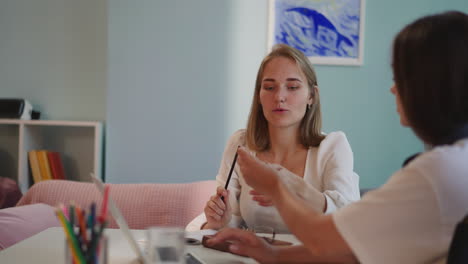 Brunette-woman-hands-red-pencil-to-friend-sitting-at-table