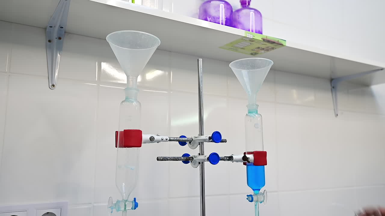 Scientist pours blue liquid into reservoir. Liquid goes to the glass tube right onto the diaper. Researcher's hand holds the timer to check the time of absorbing.