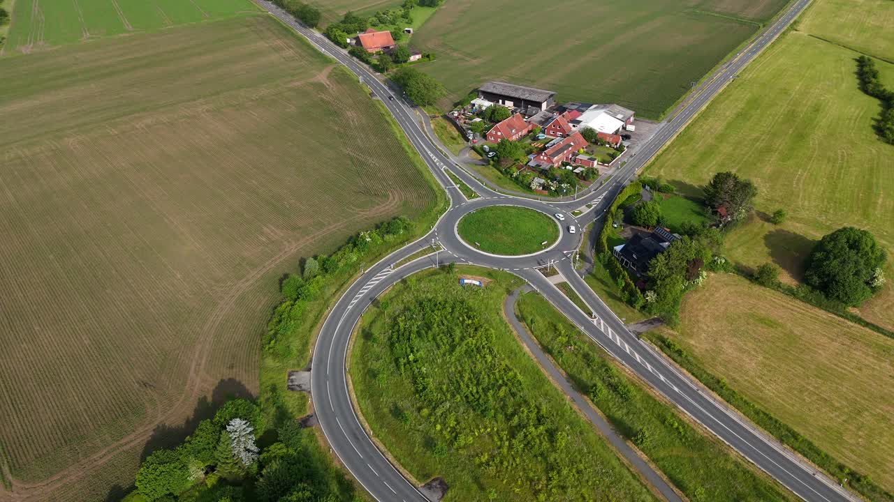 Traffic on new build roundabout in american rural countryside. Aerial top down shot. Green cropland agricultural fields in Summer. Farmstead house in brick design. Wide shot.